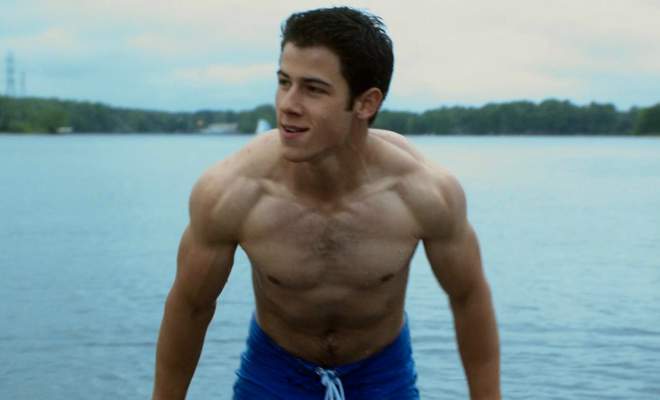 A photo of Nick Jonas shirtless climbing out of a lake.