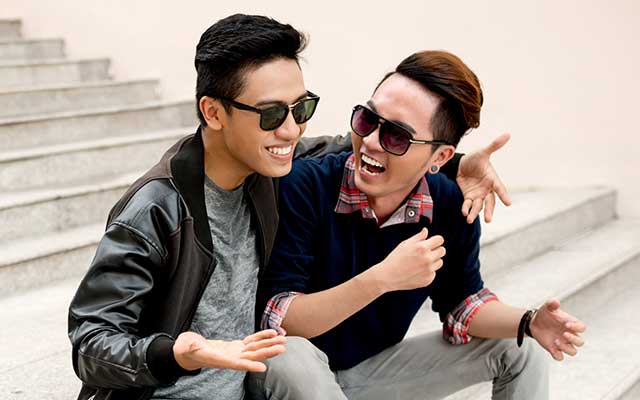 Two Asian men sitting on steps and laughing.