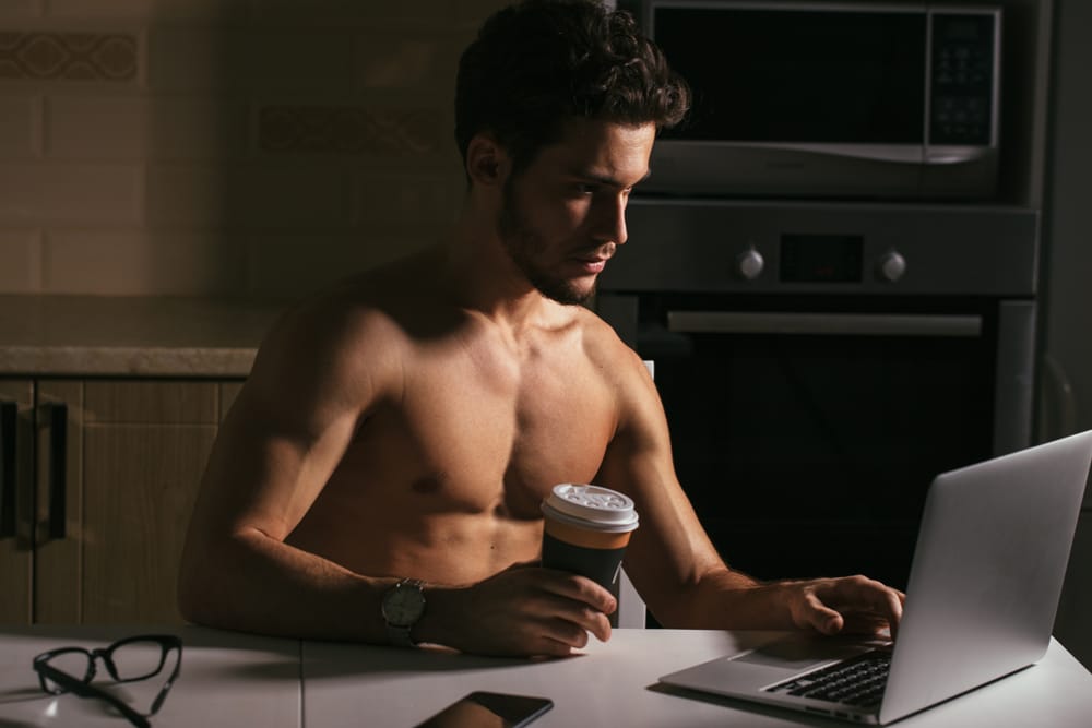 A shirtless young man working on a computer