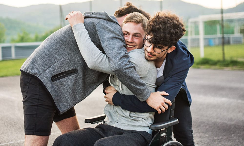 A handsome boy in wheelchair with teenager friends doing sport outside.