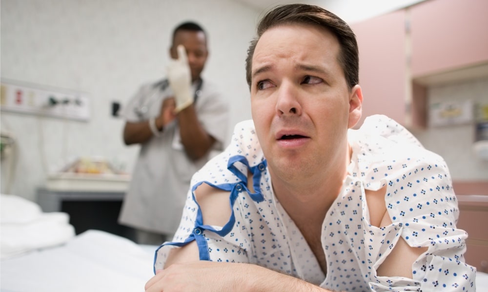 A nervous patient lying on the bed with a doctor putting on latex gloves in the background