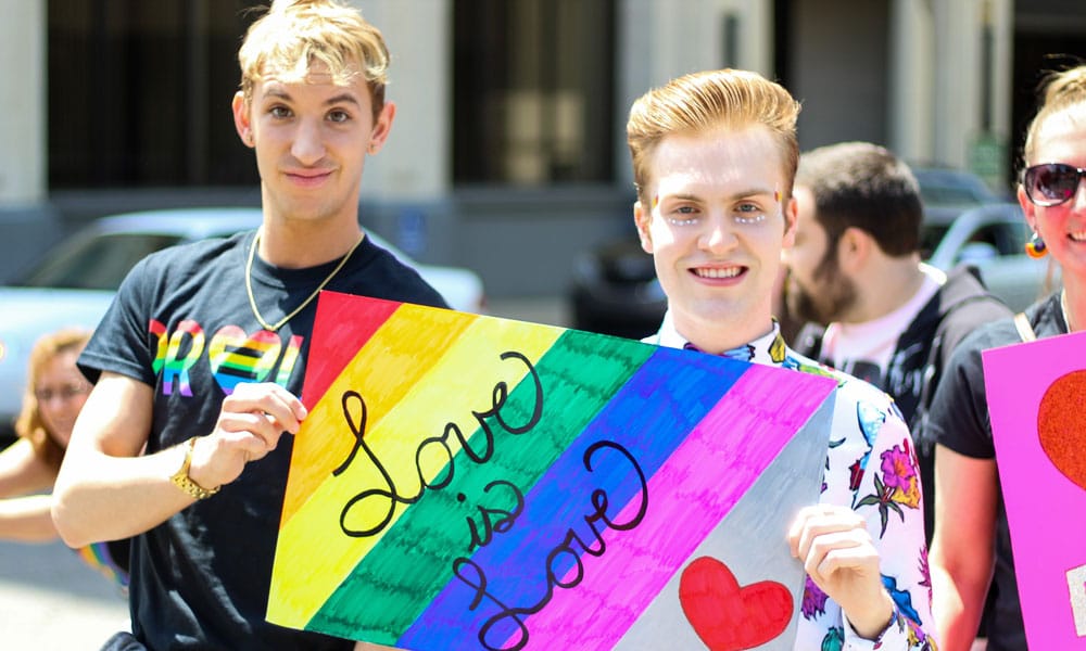 Three Men Holding Assorted Painted Love Is Love Banner