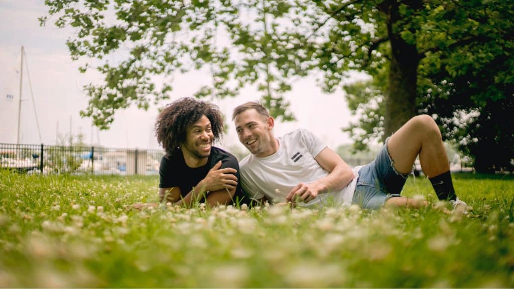 Smiling men lying on grass.