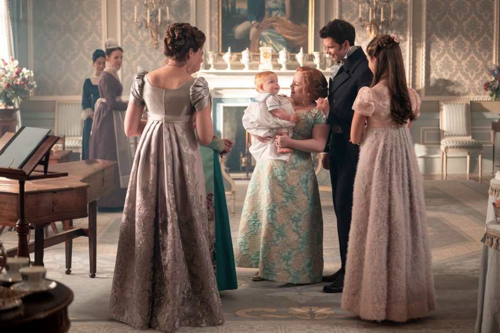 Penelope Bridgerton proudly holds her newborn baby while surrounded by her loved ones, including Colin, Violet, and Francesca Bridgerton.